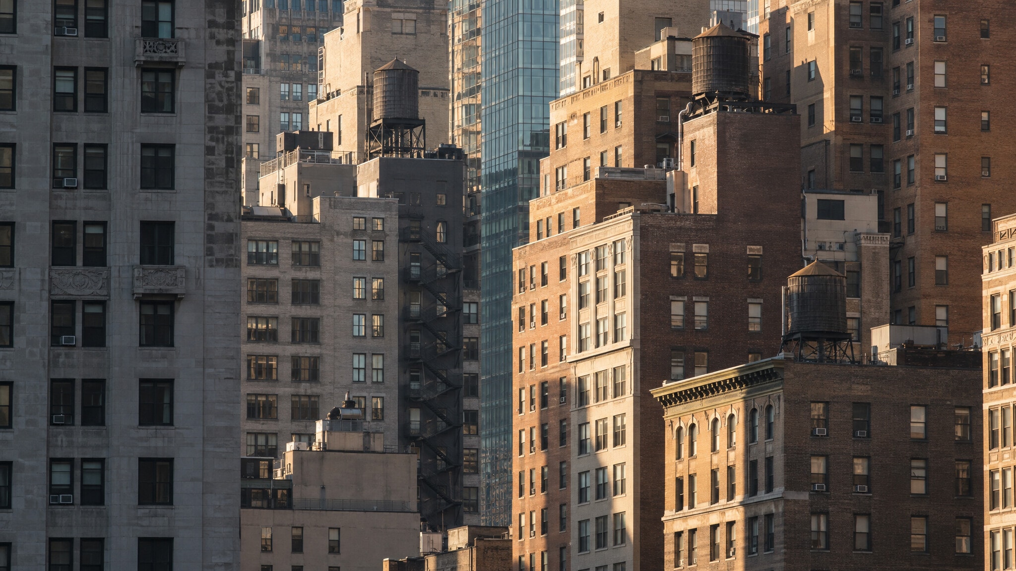 A dense wall of stone and brick city buildings in late sun, seen from across the street